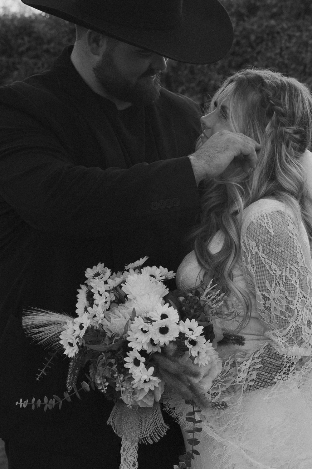 A black and white photo of newlyweds sharing an intimate moment with white floral bouquet.