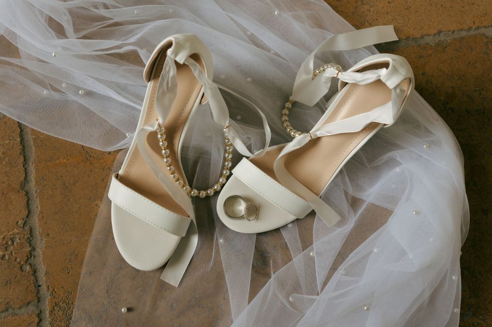 White bridal shoes with delicate bows and straps arranged on a textured surface.