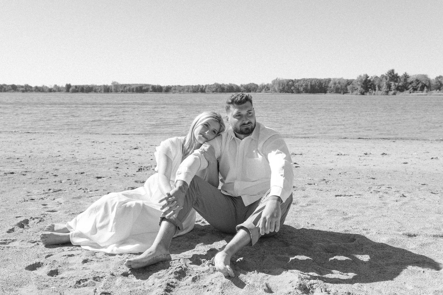 Black and white photo of couple sitting together on beach.