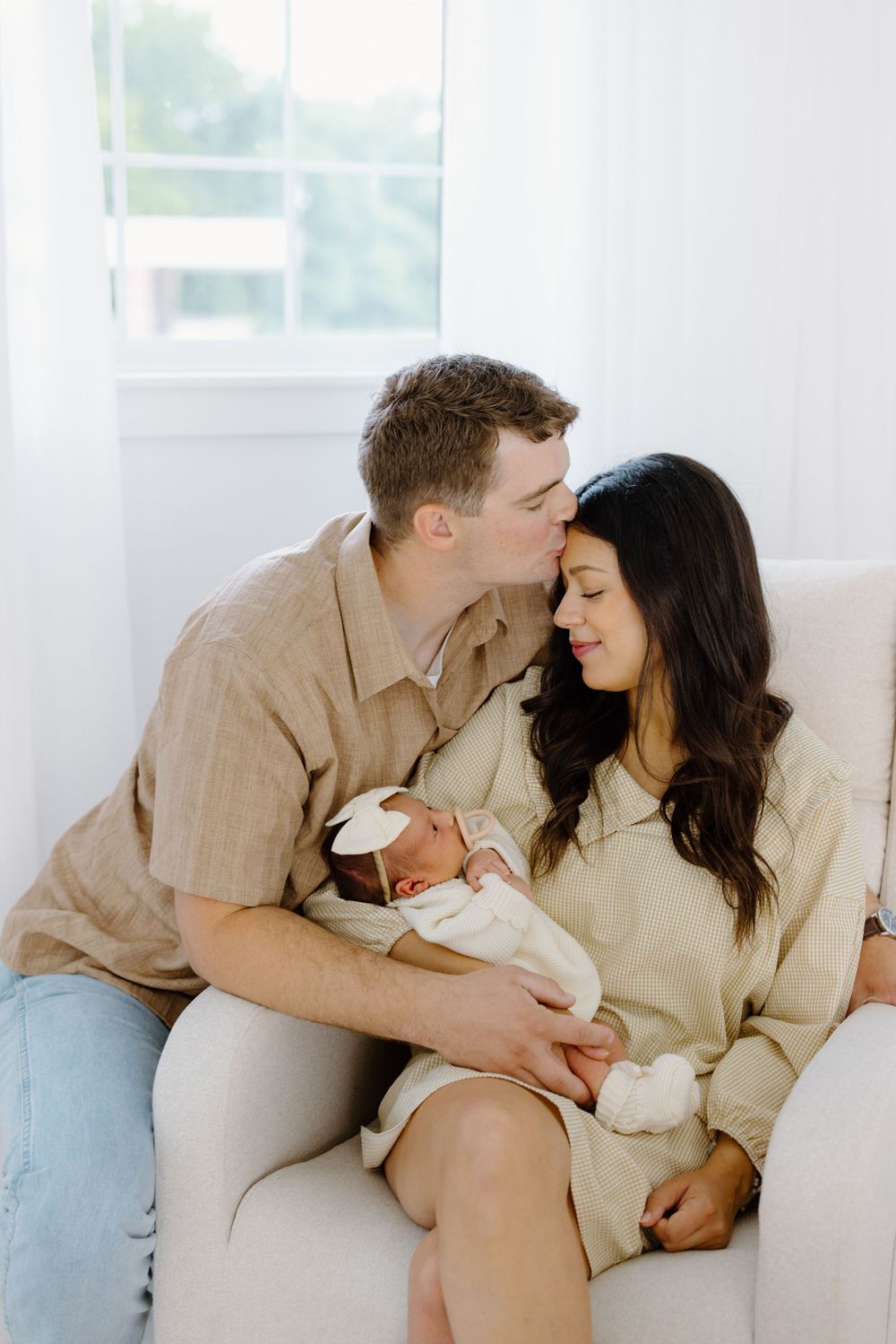 A couple shares a tender moment, with the man kissing the woman's forehead as she holds their newborn baby.