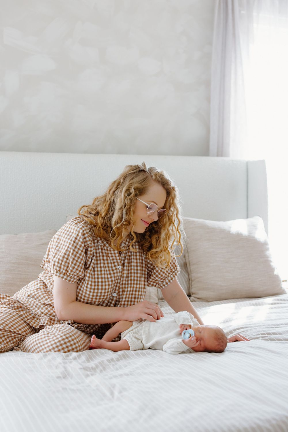 A parent in a checkered shirt lies on a white bed with a newborn baby in a series of tender moments.