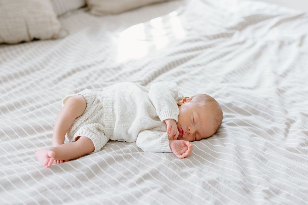 A sleeping newborn baby lies peacefully on white bedding in a series of connected photographs.