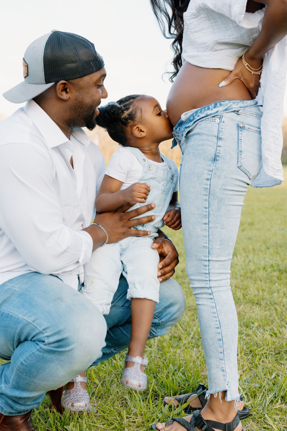 A touching outdoor family moment with casual denim and white outfits on a grassy lawn.
