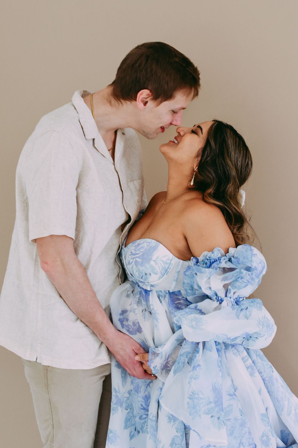 A couple shares an intimate romantic moment while wearing a white shirt and flowing light blue floral dress.