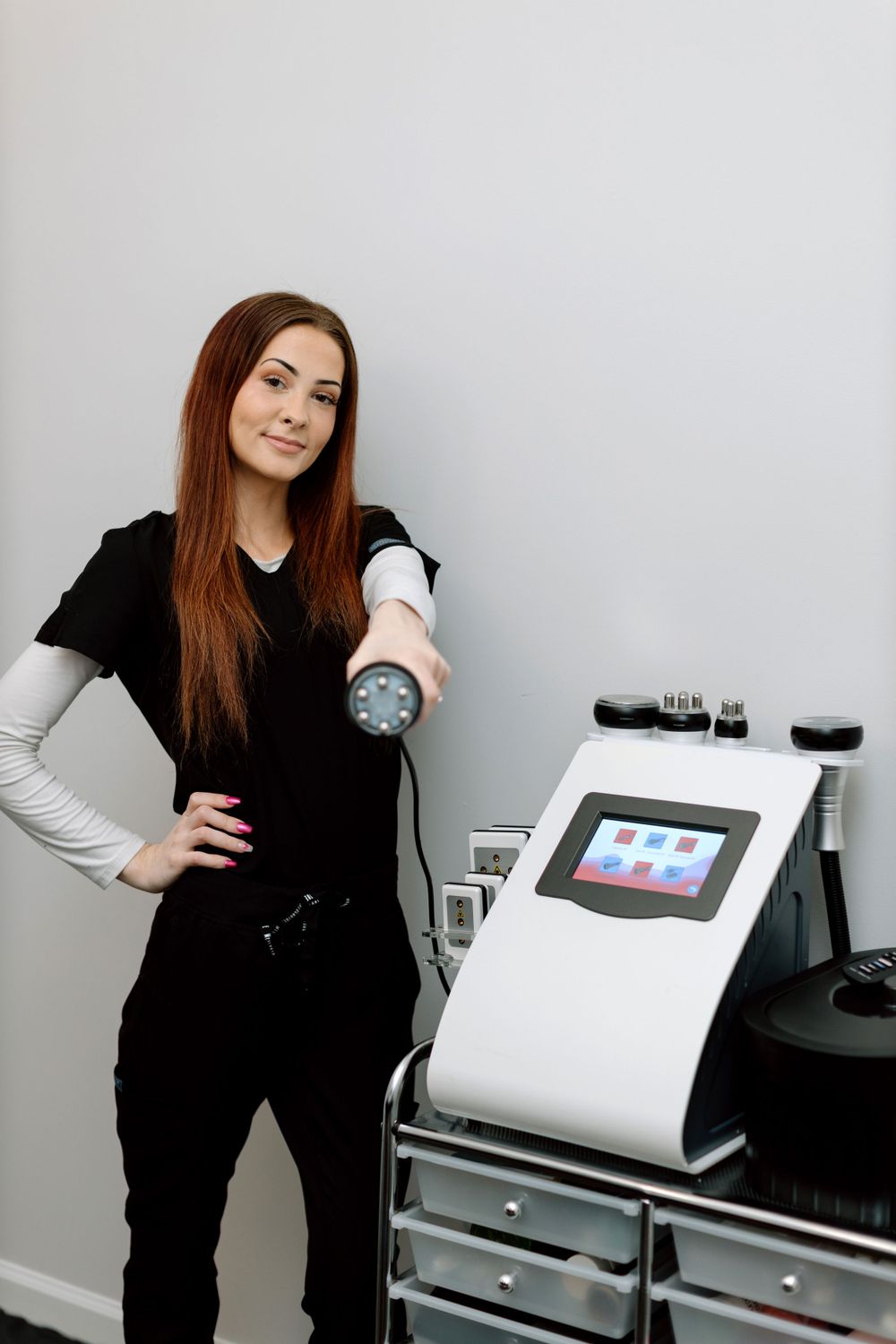 Medical aesthetician standing beside a modern skincare treatment device with digital display in a professional clinic setting.