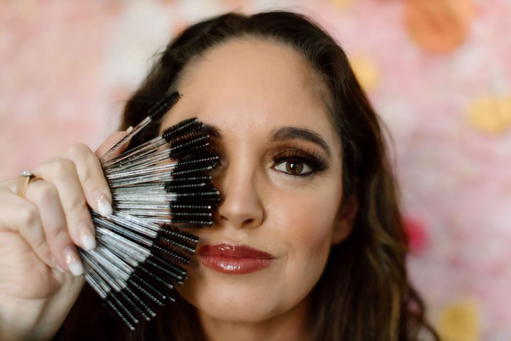 Close up of makeup brush collection being held near smokey eye and red lipstick look against pink background.