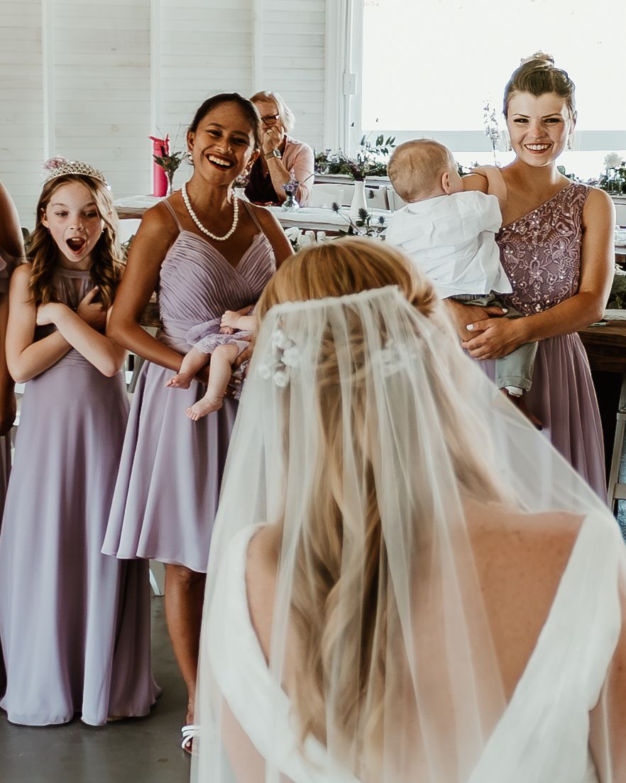 Wedding party members in purple dresses share joyful reactions during a candid moment.
