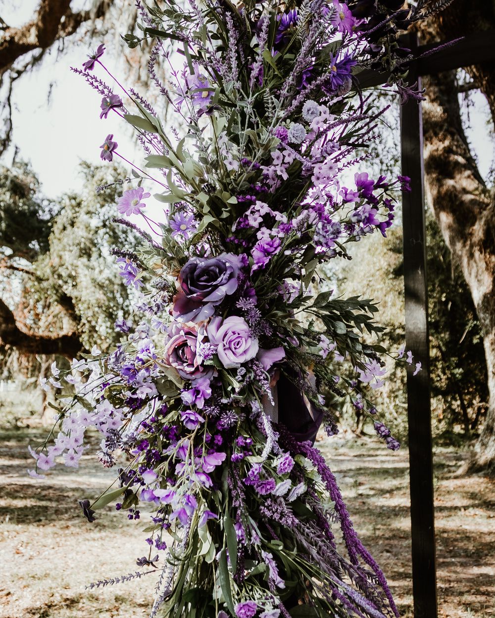 Purple floral wedding decorations adorning outdoor venue with natural lighting.