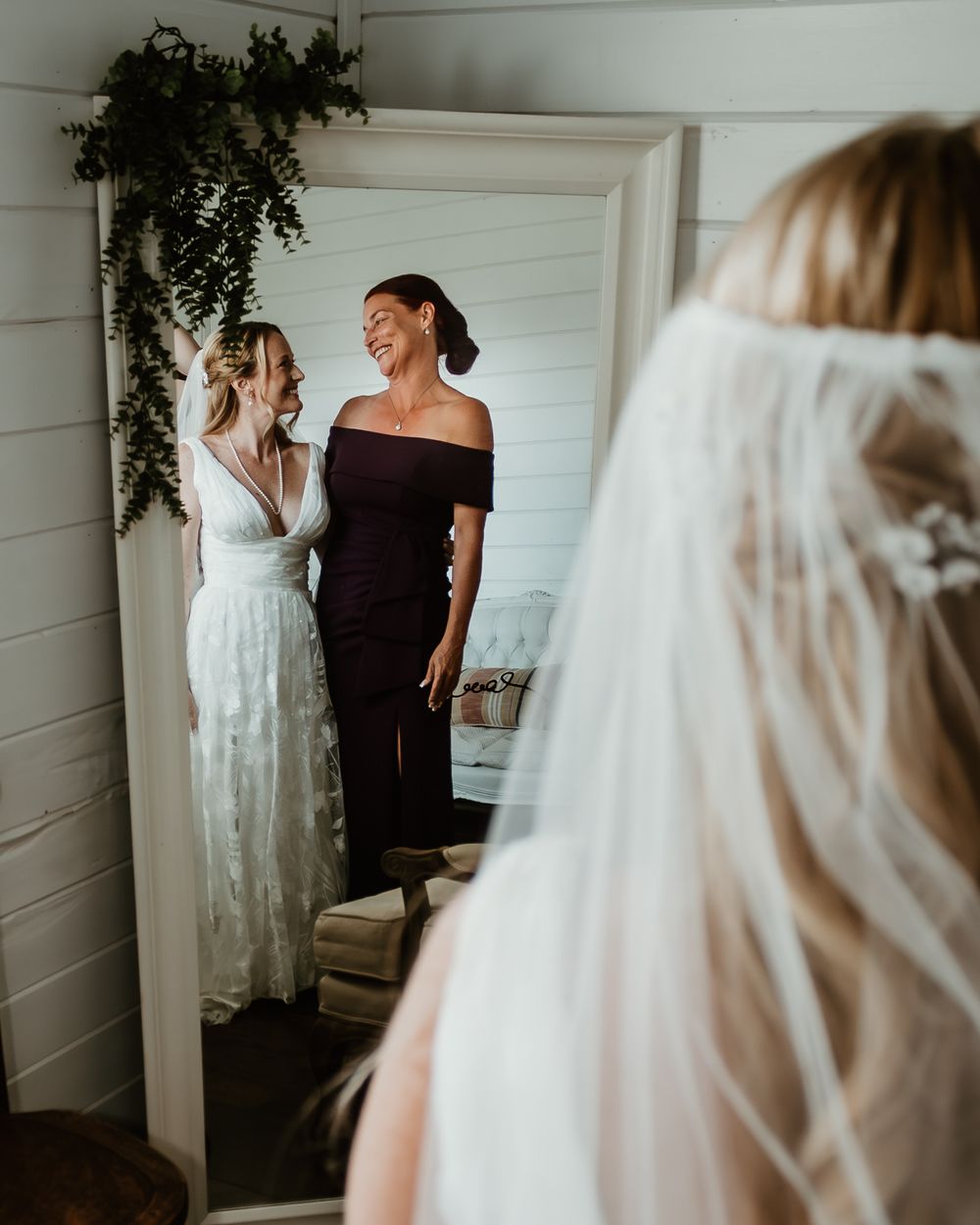 Final wedding dress adjustments in white room with hanging greenery.