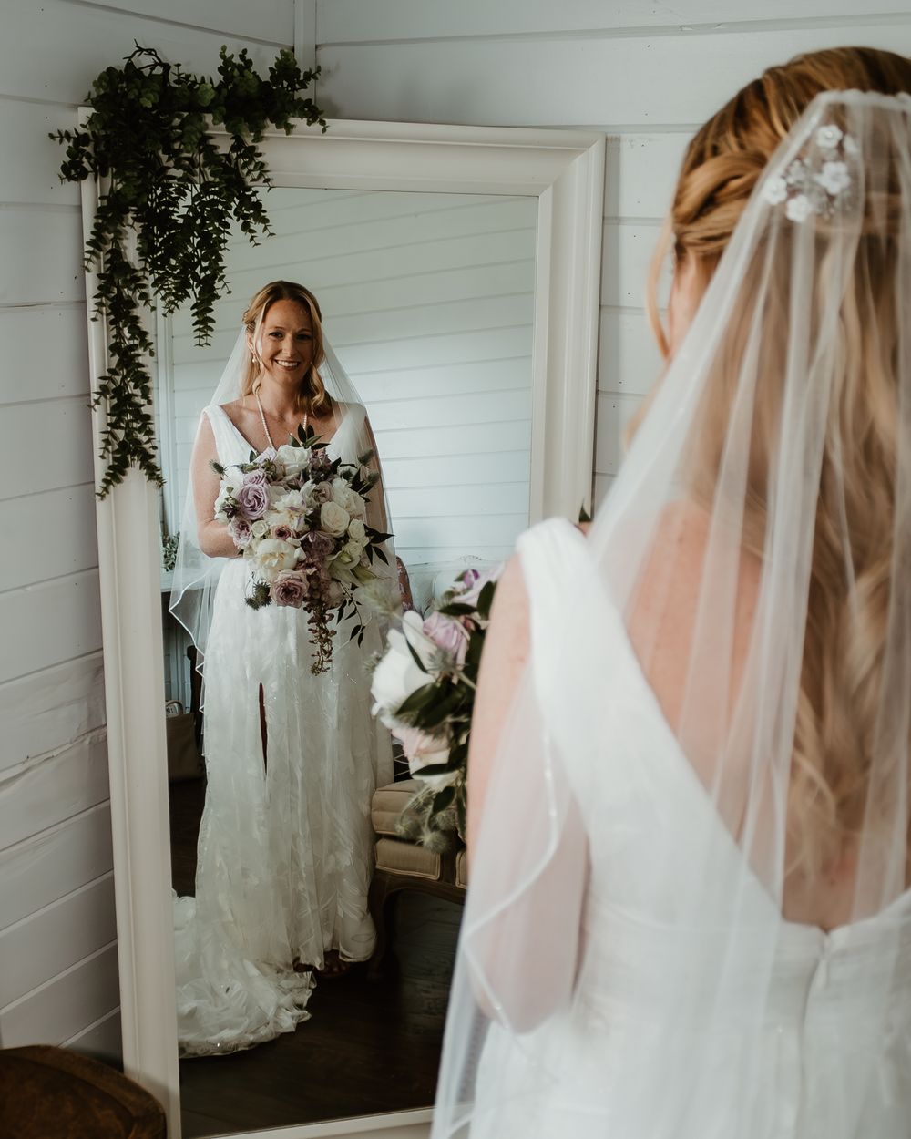 Bride in lace wedding gown with flowing veil in white room.