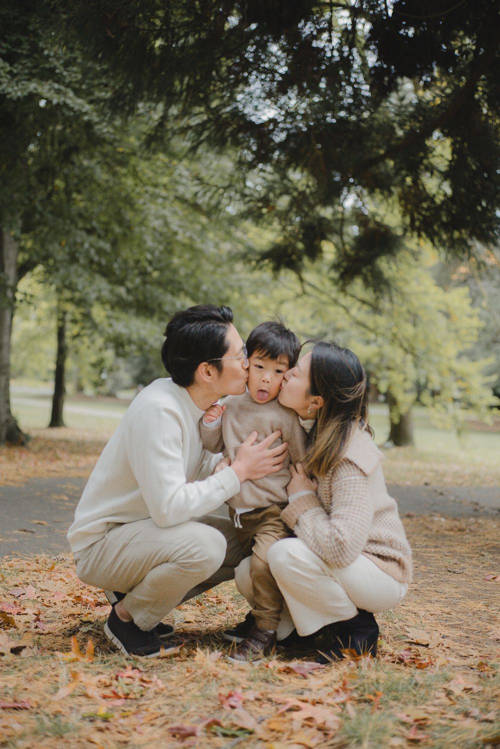 Family sharing tender moments together while sitting on fallen autumn leaves in a park setting.