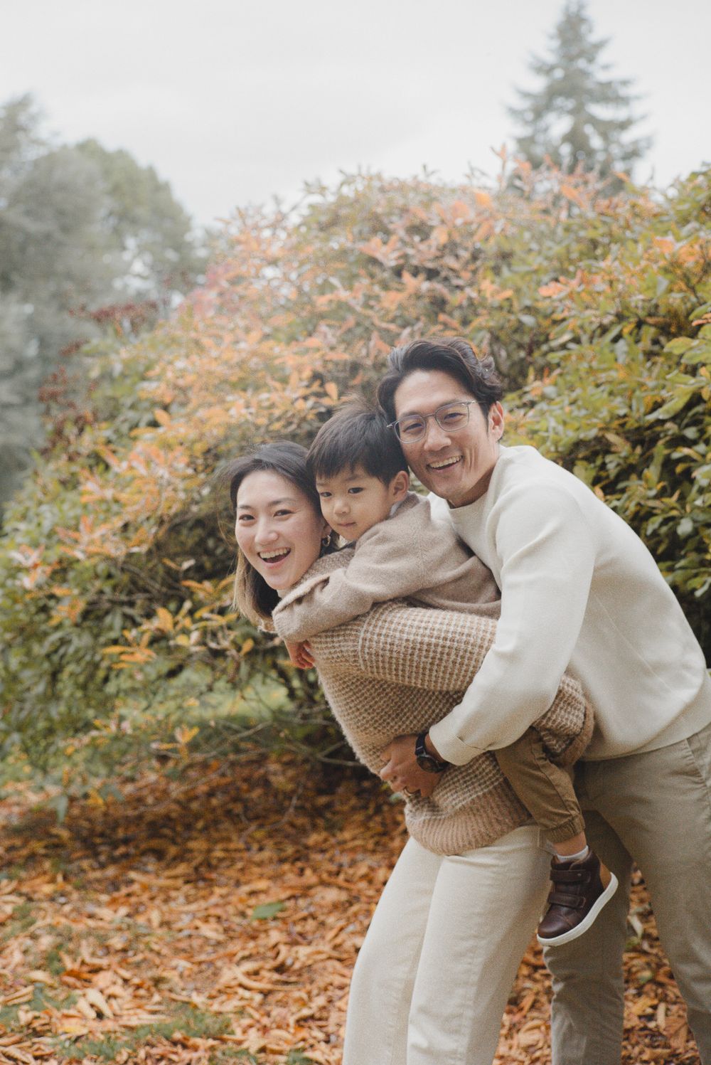 A family enjoying a playful moment together outdoors during autumn with fall foliage in the background.