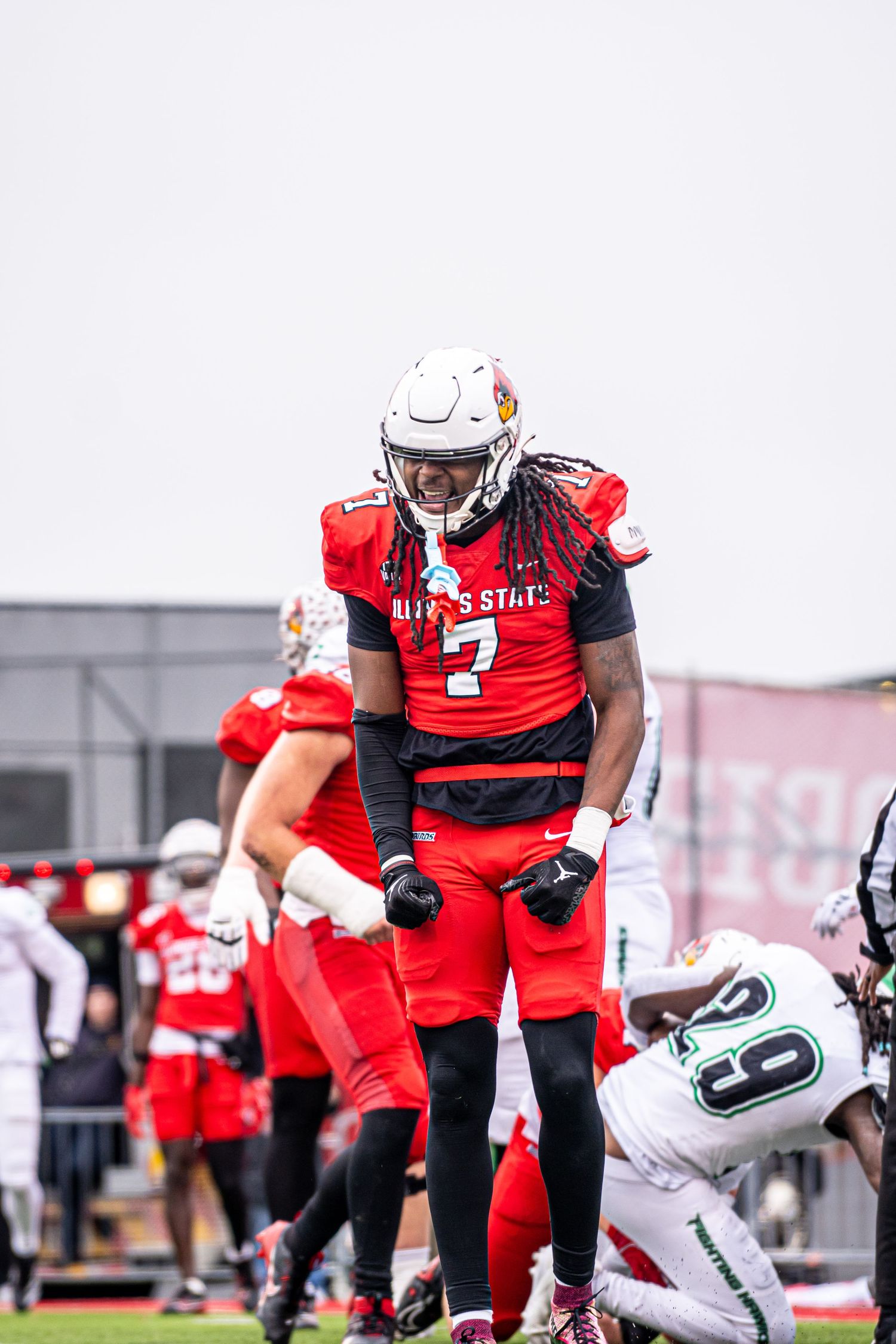 A football player in a red uniform and white helmet stands over a fallen opposing player during a game.