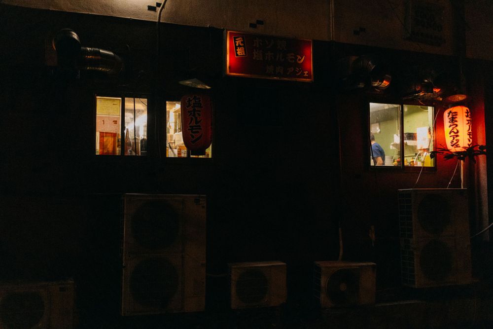 Night view of illuminated Japanese building windows with red lanterns casting warm glow.