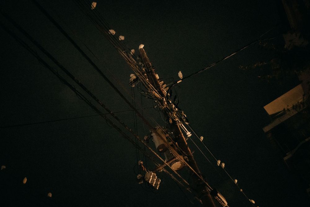 Power lines and telephone wires illuminated against a dark night sky.