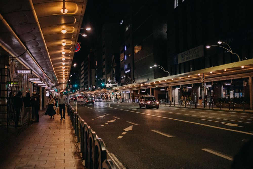 Illuminated city street at night with covered walkway and traffic lanes.