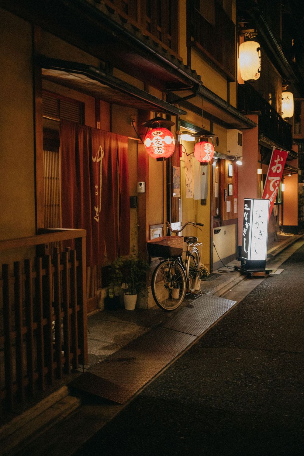 Cozy Japanese street at night with glowing lanterns and parked bicycle outside traditional shops.