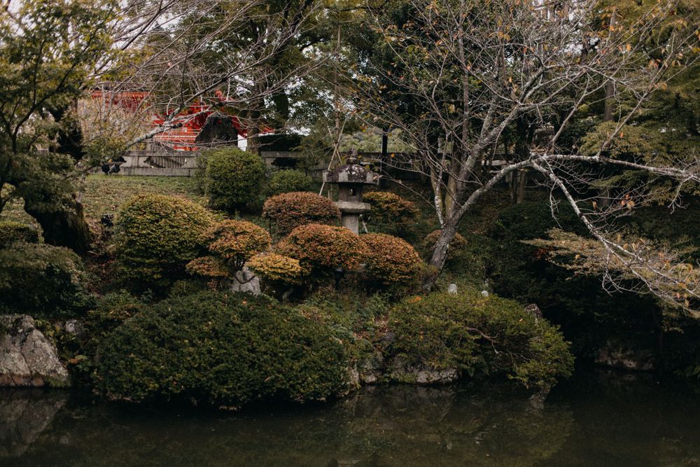 Traditional Japanese garden with mossy rocks and autumn trees beside a pond.