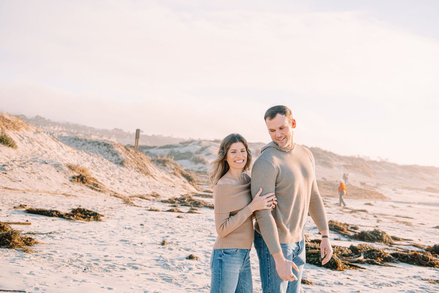 Couple in casual attire walking together on a scenic sandy beach during golden hour.