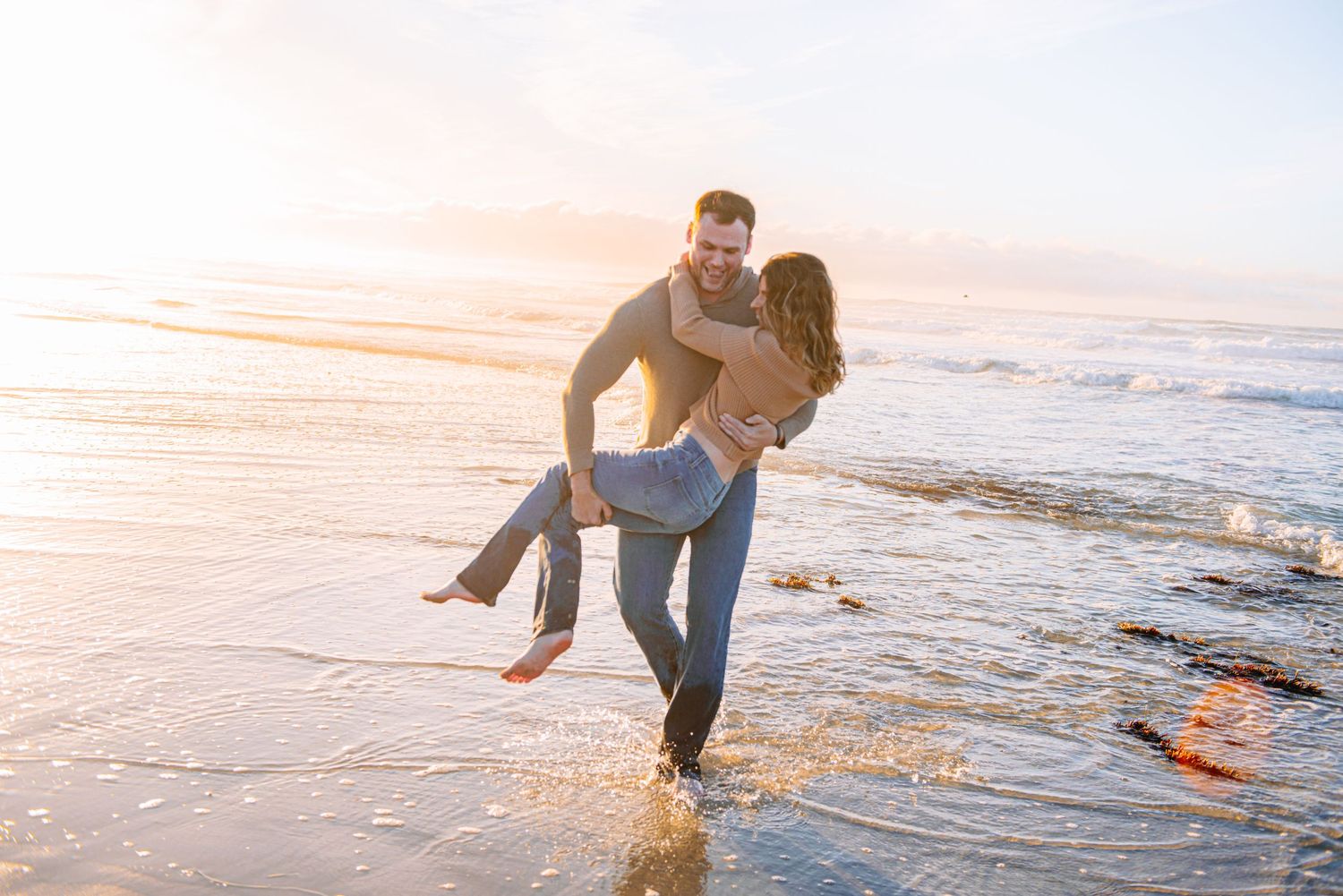 A couple playing and splashing in the waves at sunset on a romantic beach getaway.