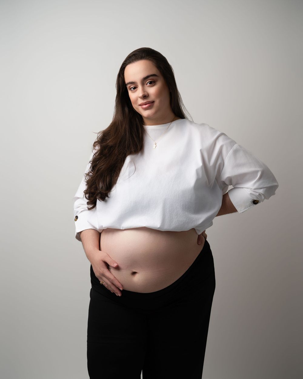 Pregnant woman in white crop top showing baby bump in professional maternity portrait.