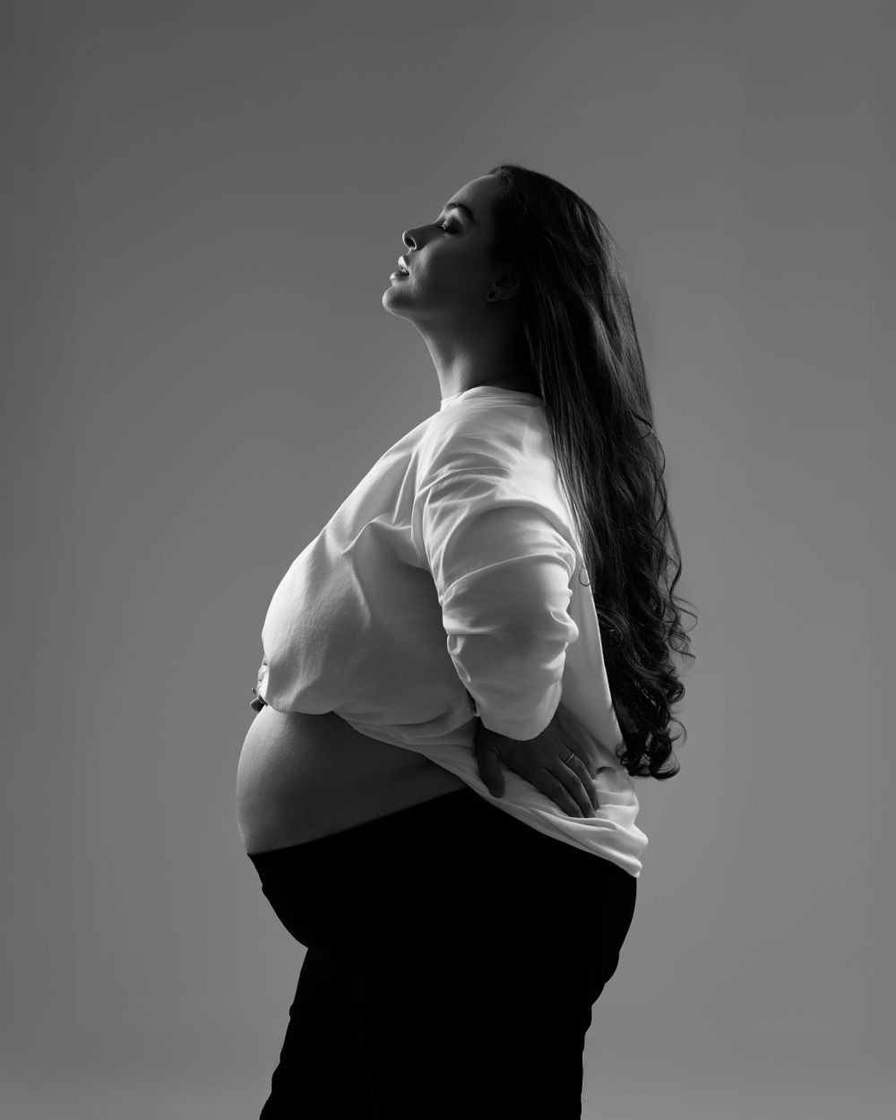 Black and white side profile of pregnant woman in white shirt looking up, maternity photo.