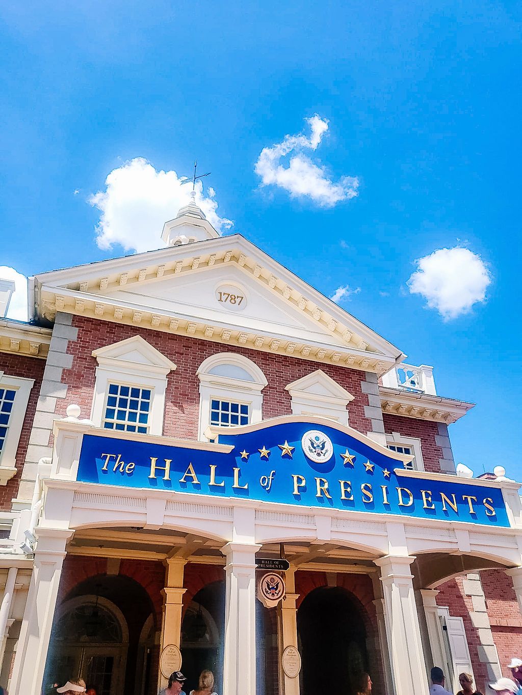 The Hall of Presidents attraction building at Walt Disney World features brick and white columns under a bright blue sky.
