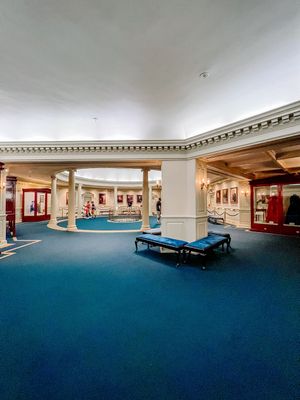 Grand hotel interior with blue carpeting, elegant columns, and luxurious lounge seating in a curved corridor design.