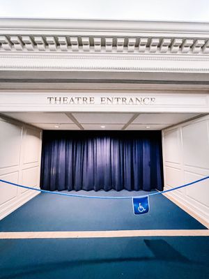 A classic theatre entrance with ornate white molding and dark navy blue curtains spanning across an archway.