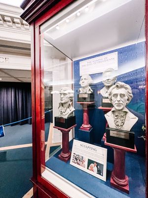 Museum display case showing white classical busts and artifacts with red framing and blue background panels.
