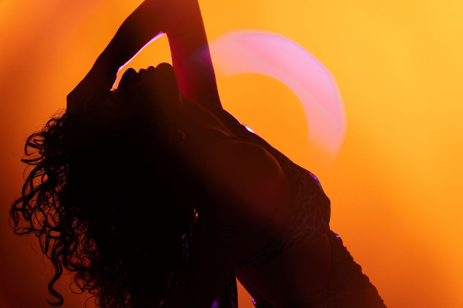 Silhouette of a figure with curly hair stretches against vibrant orange sunset sky with pink sun in background.