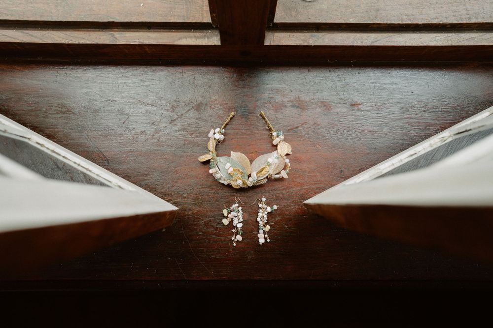 Wedding jewelry including delicate pearl earrings and a floral headpiece displayed on dark wooden surface.