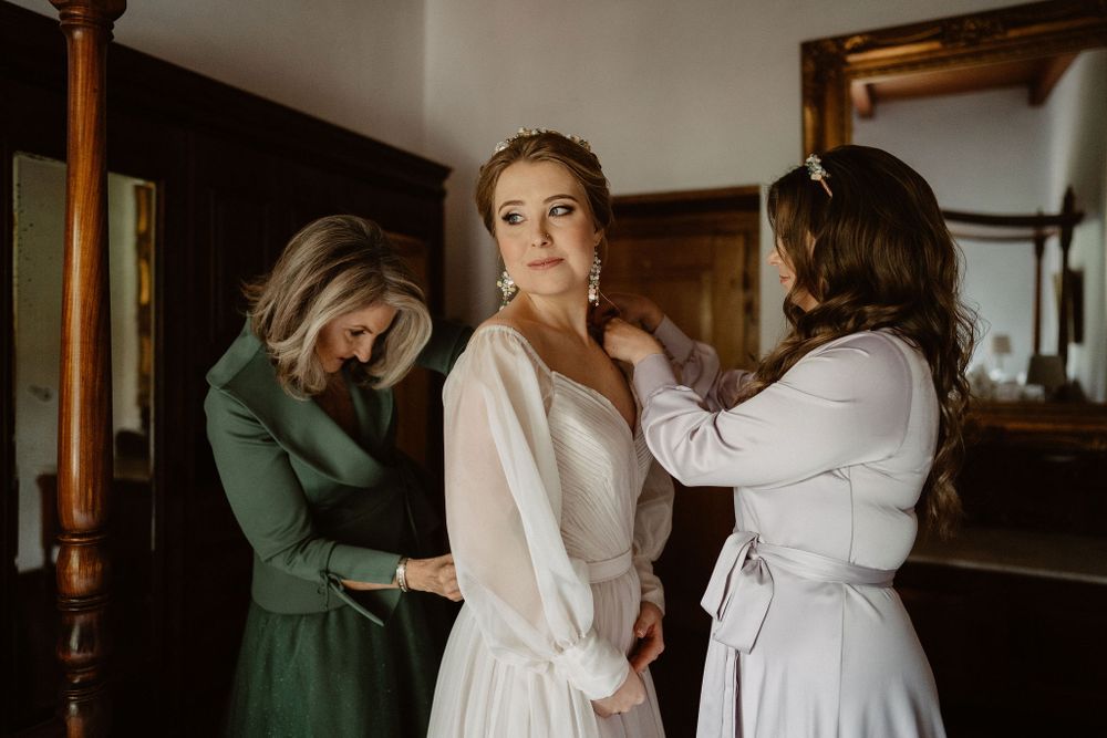 Bridesmaids in green dresses help the bride get ready in a morning preparation scene with natural light.
