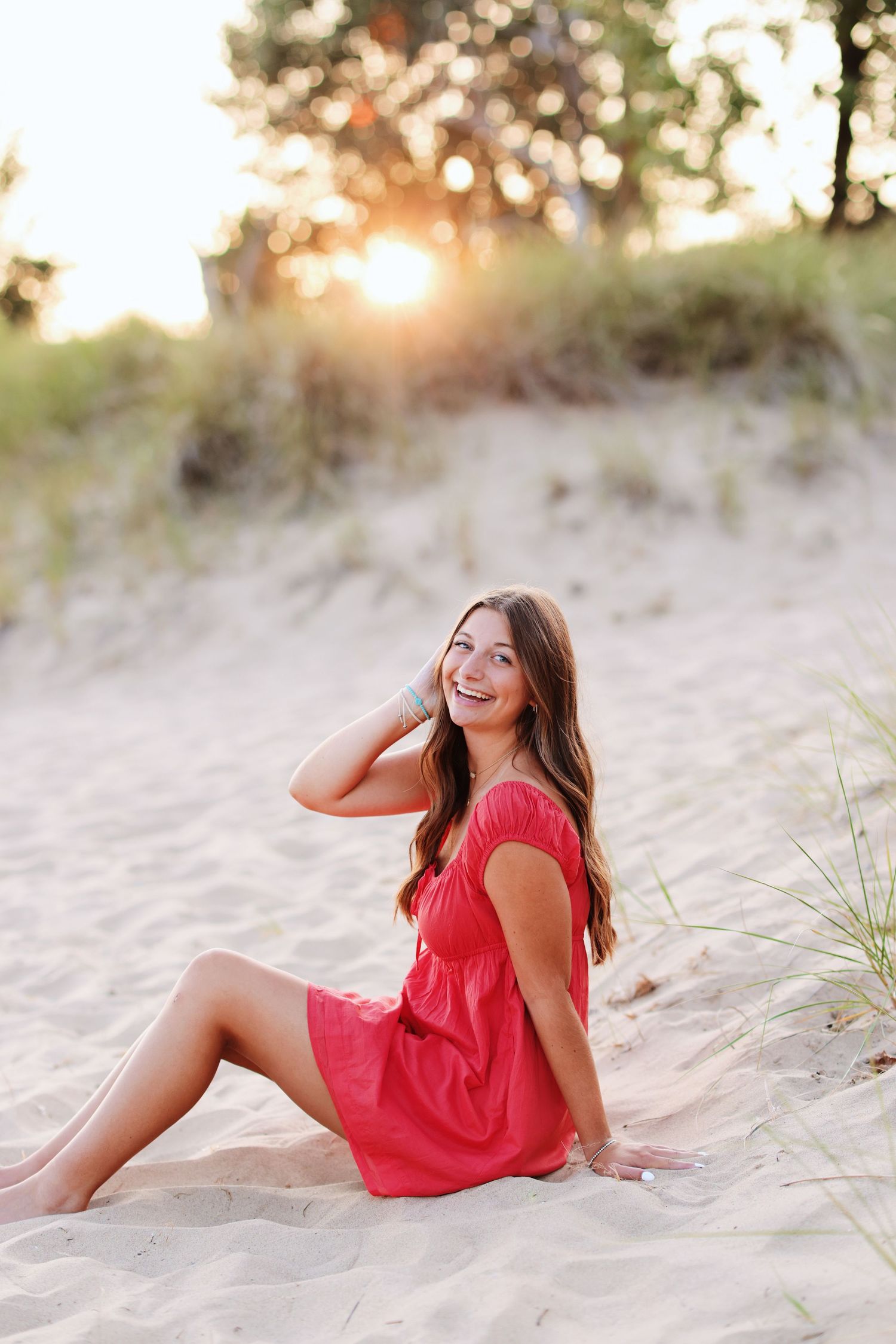 Person in red dress sitting on sandy beach at golden sunset.