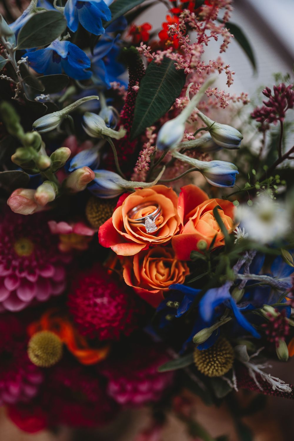 Close-up of vibrant orange roses and blue flowers in a wedding bouquet arrangement.