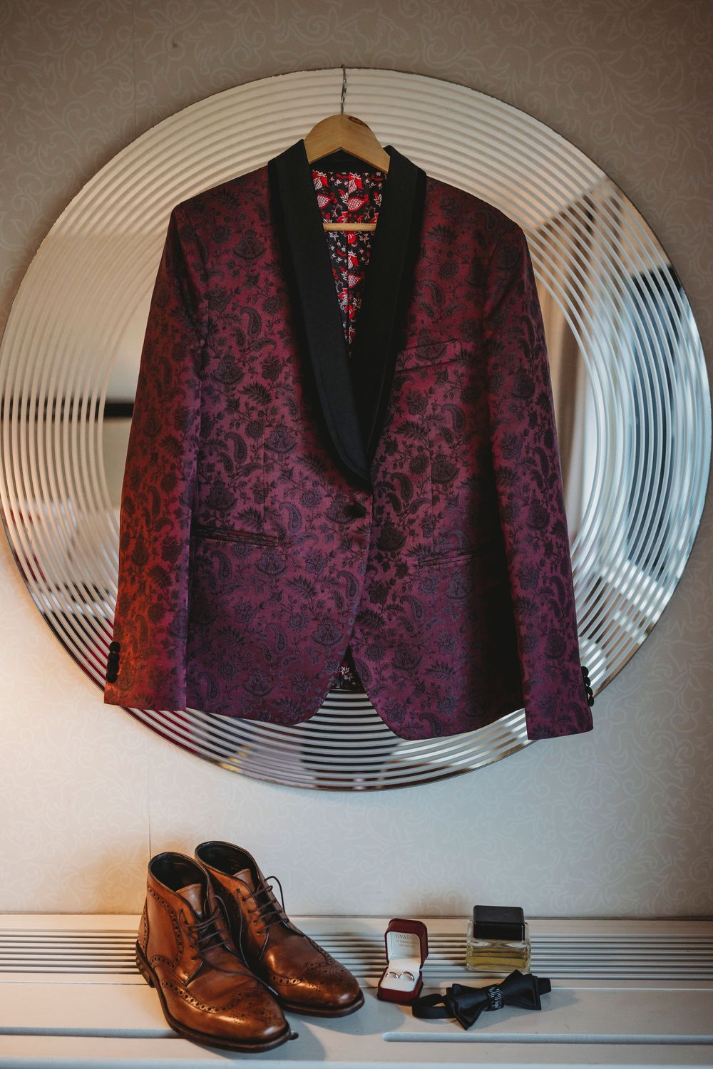 Burgundy brocade tuxedo jacket with black lapels displayed with brown leather dress shoes and accessories.