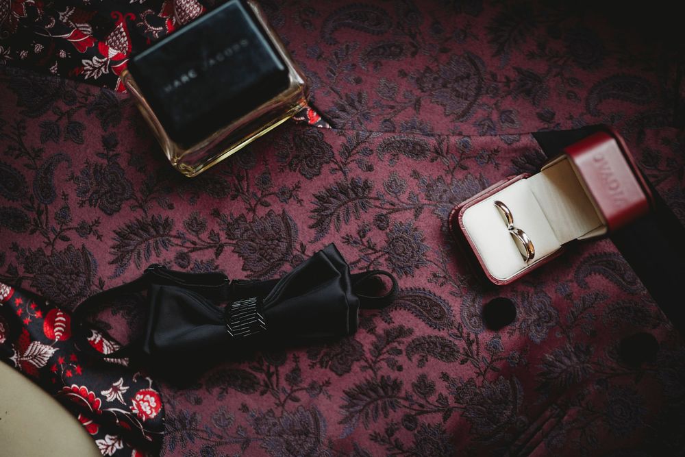 Wedding accessories including bow tie and ring box on dark floral pattern background.
