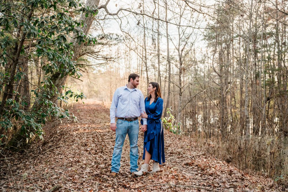 Couple walking together on leaf-covered path through winter woods.