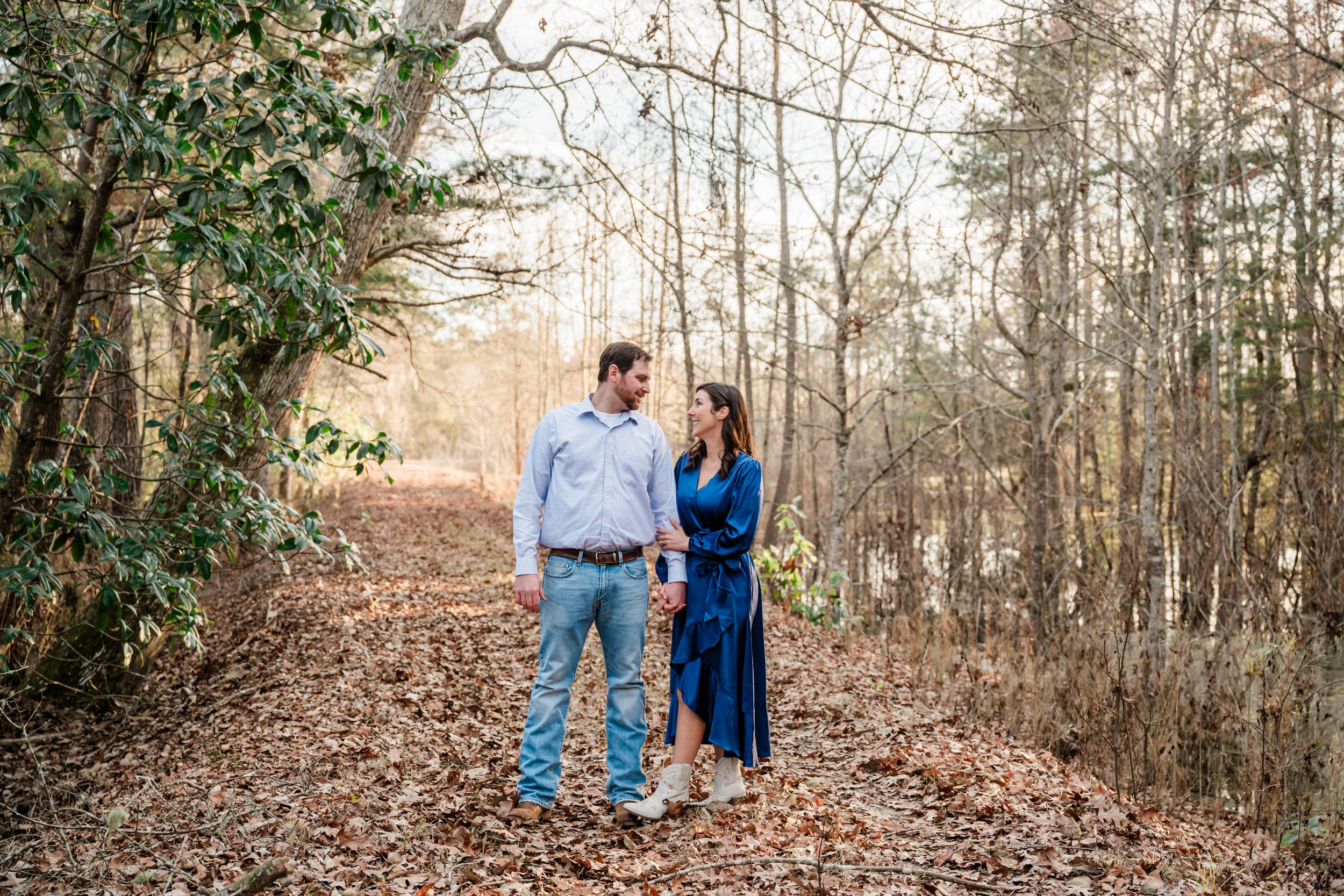 Couple walking together on leaf-covered path through winter woods.