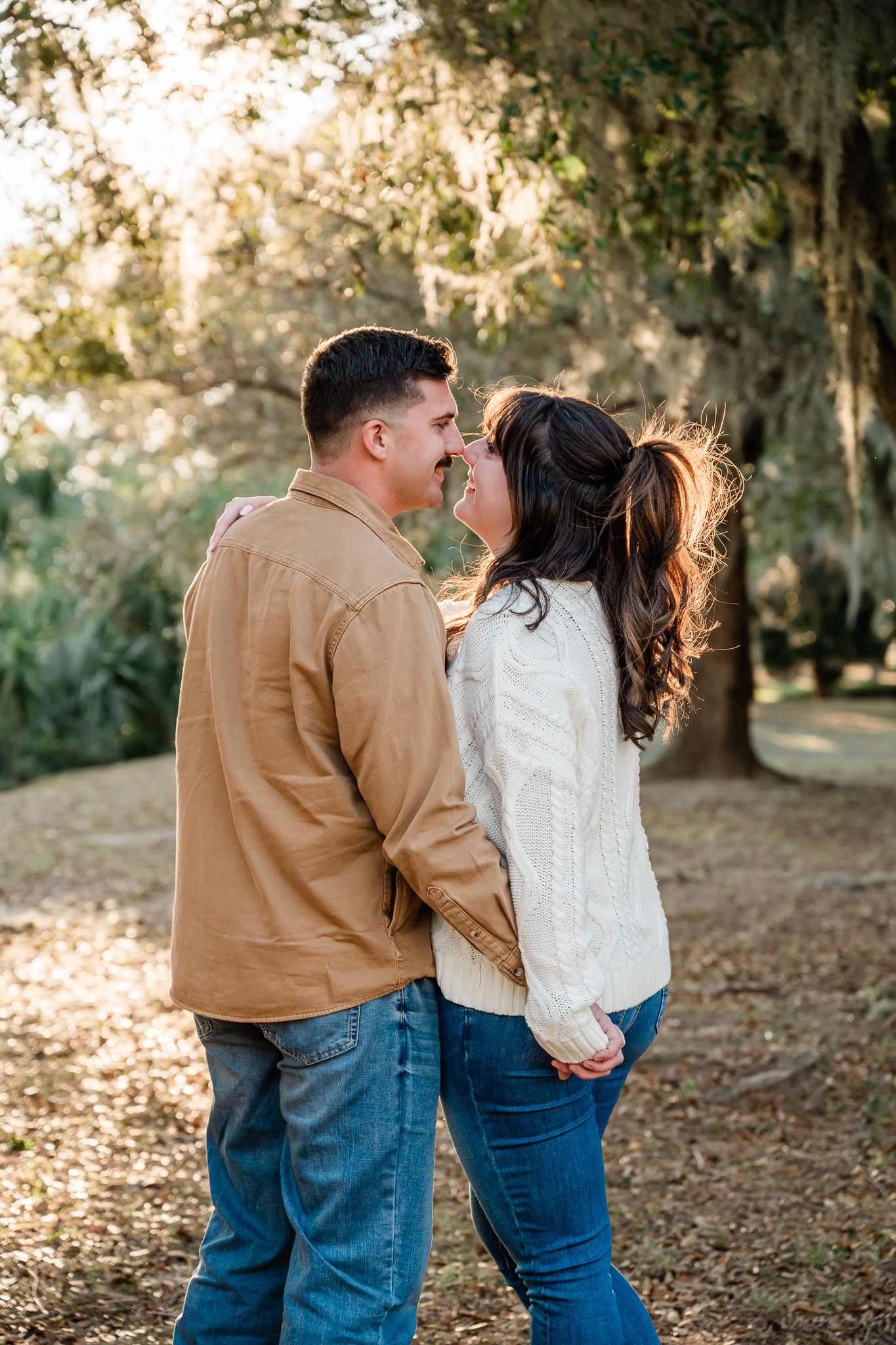 Couple sharing an intimate moment outdoors among trees during golden hour.