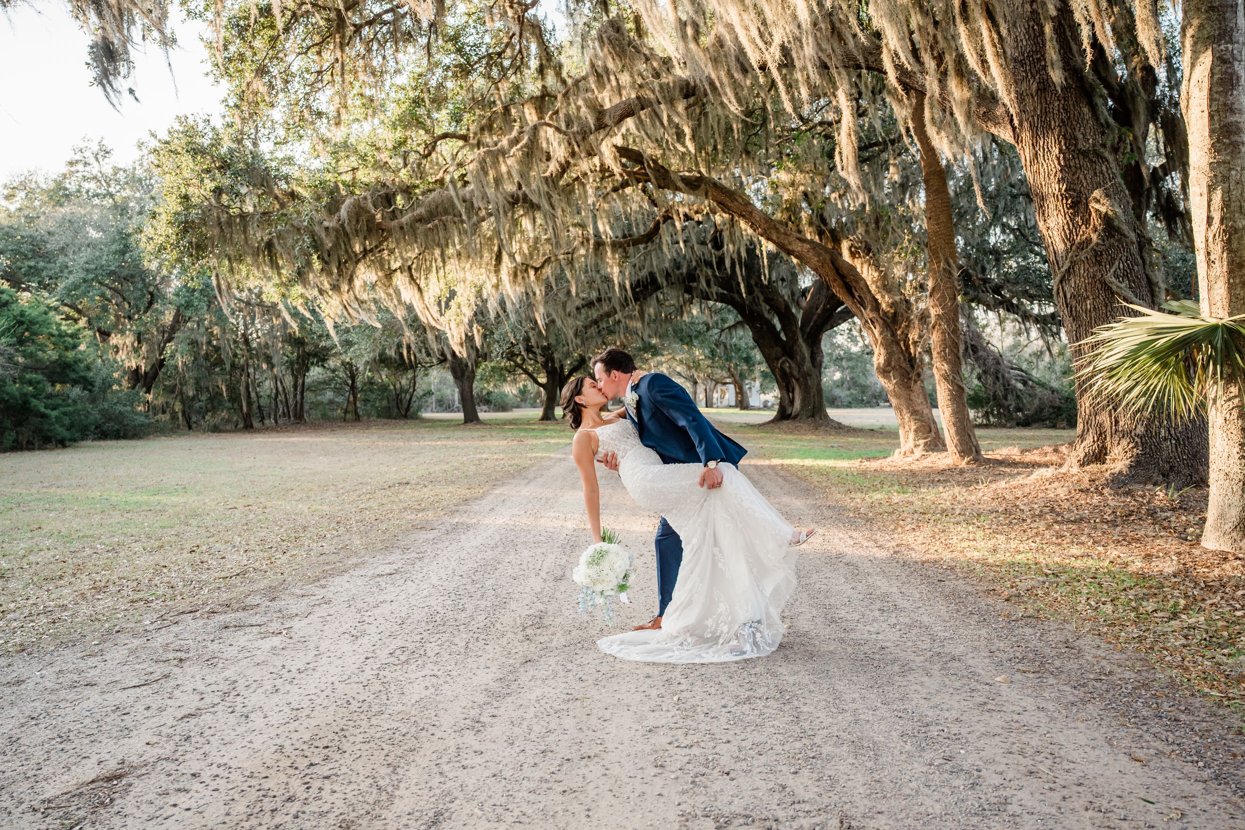 Wedding couple sharing romantic moment on tree-lined dirt path.