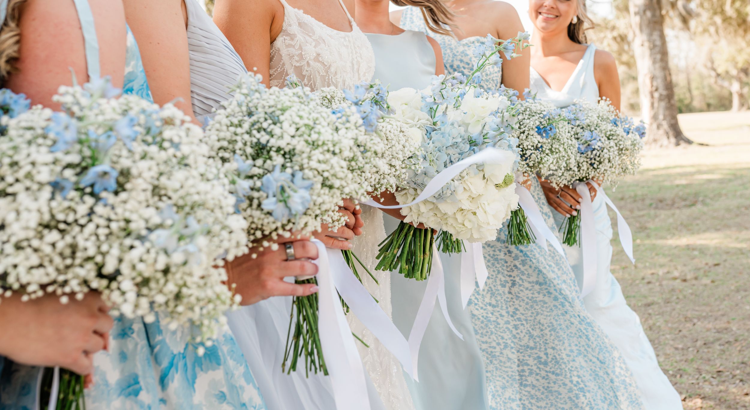 Row of bridesmaids in light blue dresses holding baby's breath bouquets.
