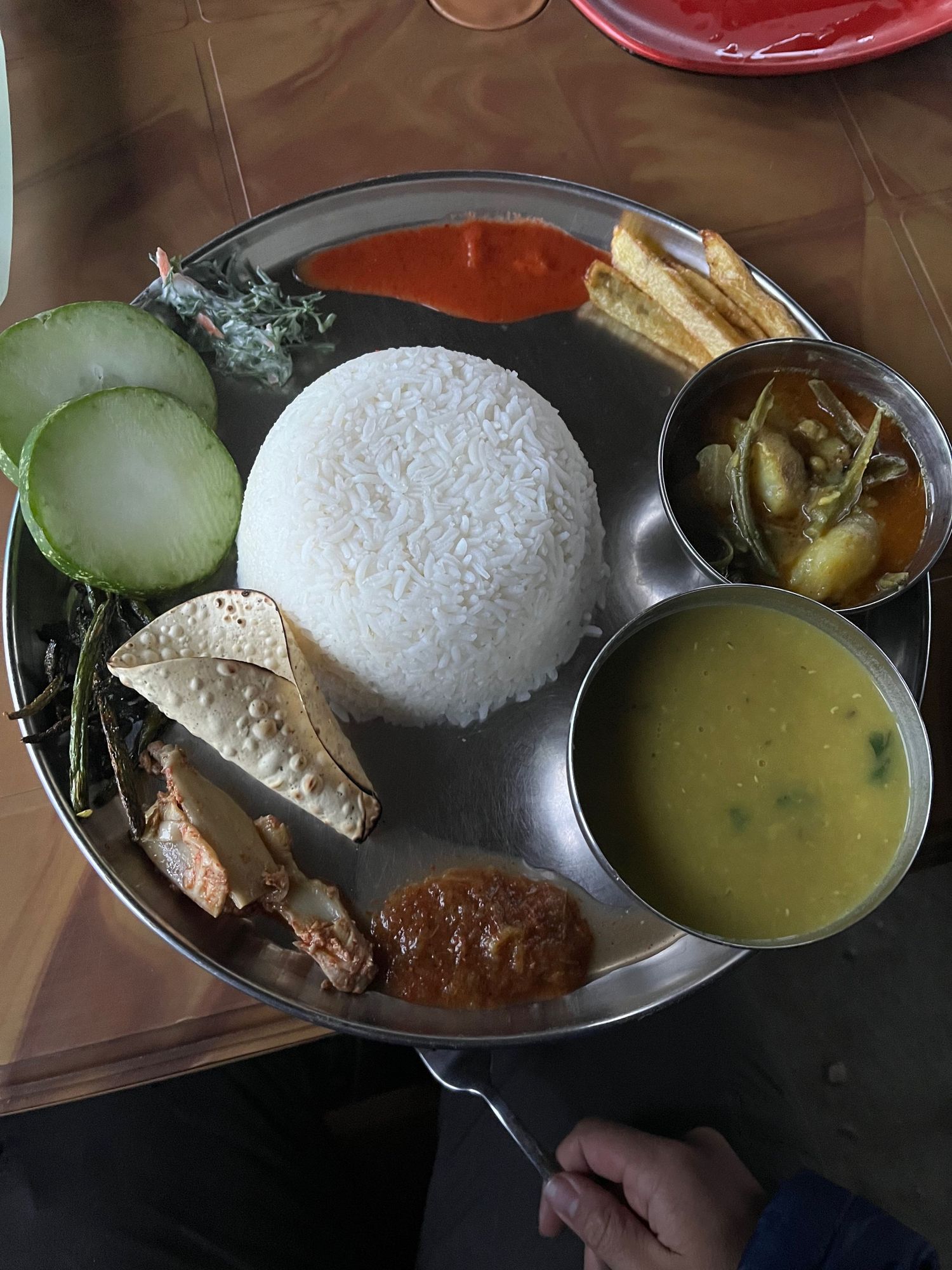 Traditional Nepalese meal served with white rice, curry, and soup in metal plates.