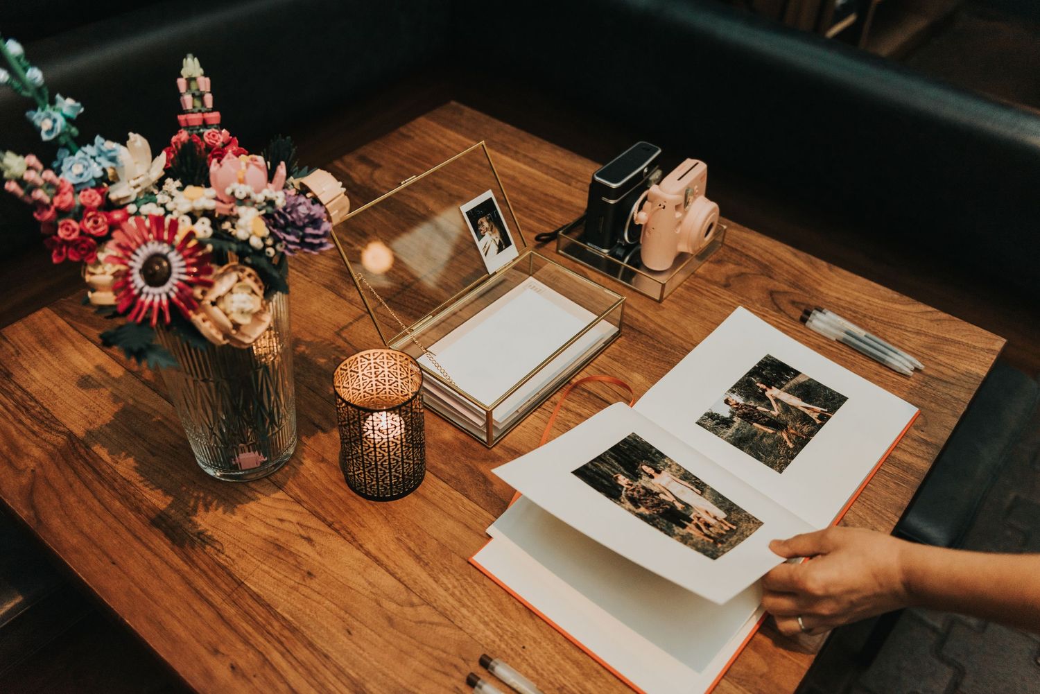 Pink flowers in a vase next to photo prints and paper on wooden table during creative session.