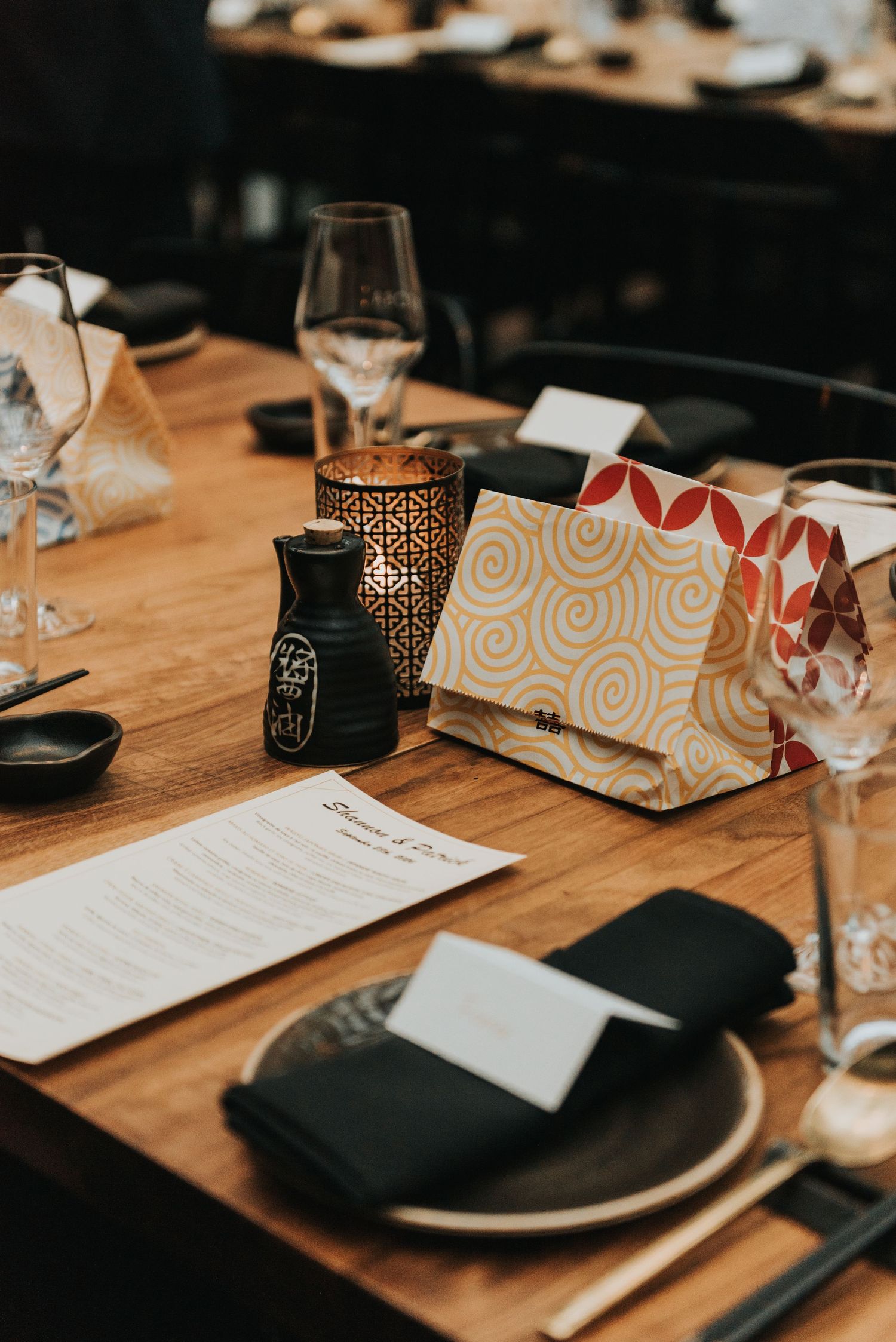 Elegant table setting at upscale restaurant with wine glasses, black plates, and decorative paper bags on wooden surface.