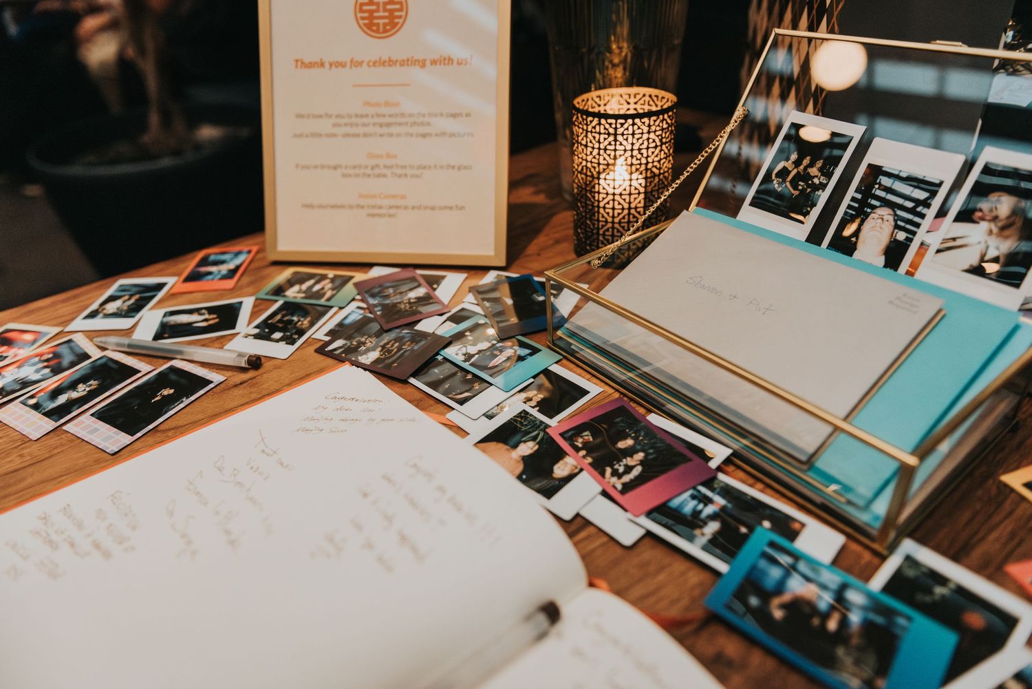 Vintage polaroid photos and photo albums scattered on wooden table with guest book and decorative lighting.