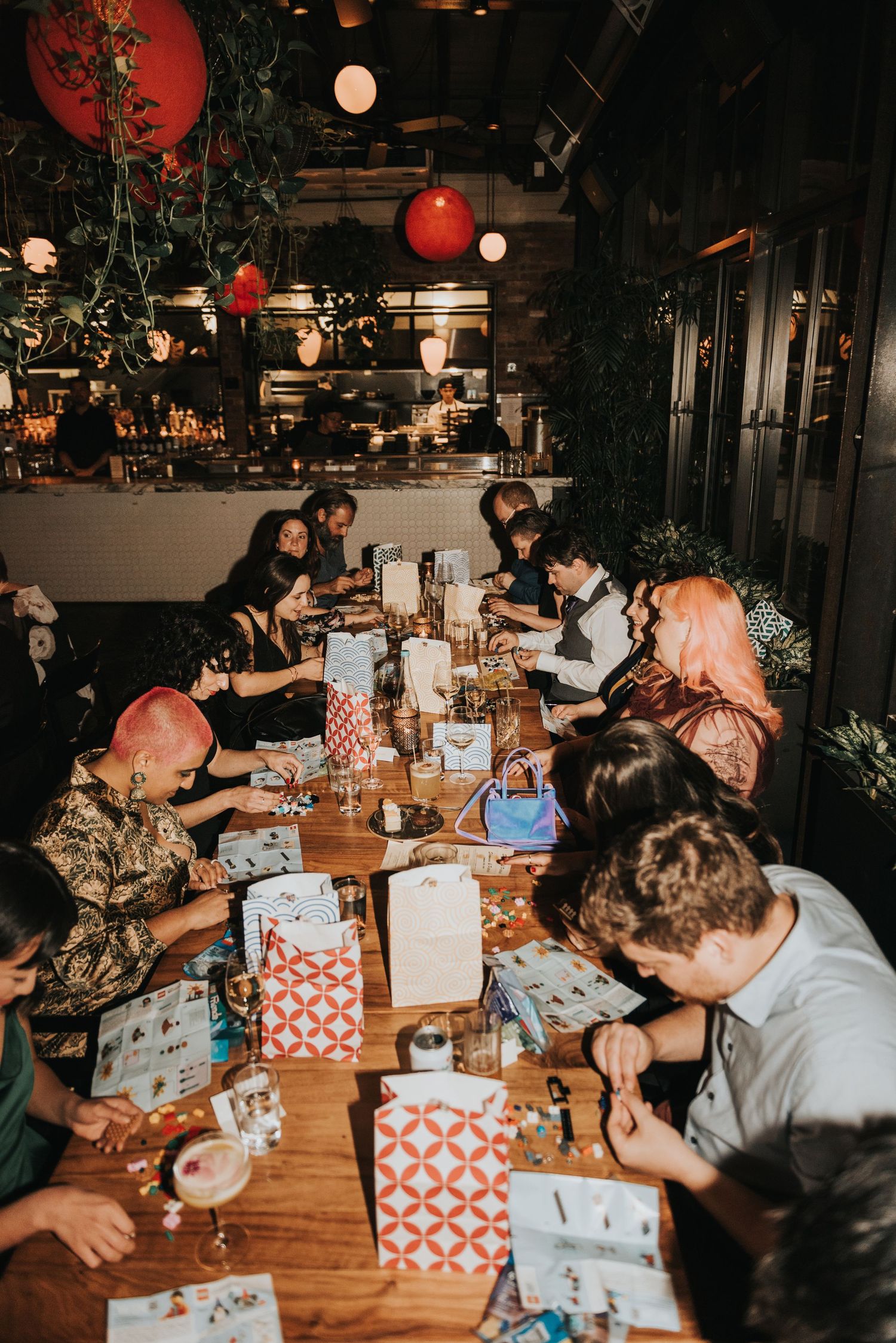 A group gathers at a dimly lit restaurant table decorated with red lanterns and gift bags for a special occasion.