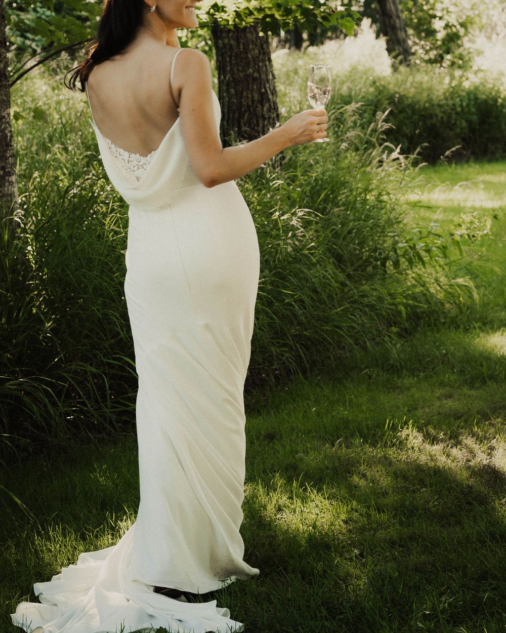 Elegant white dress flows in natural sunlight among green foliage.