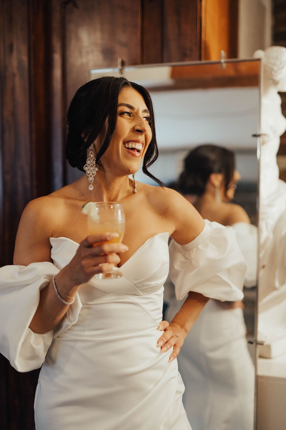 A person in a white wedding dress laughs joyfully during preparation.