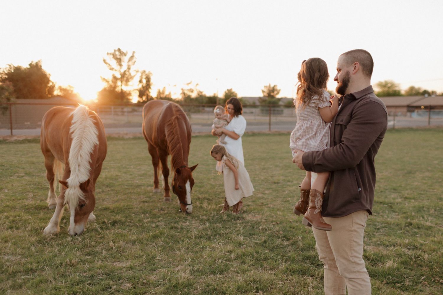 A family enjoying time together in a field with horses during sunset.